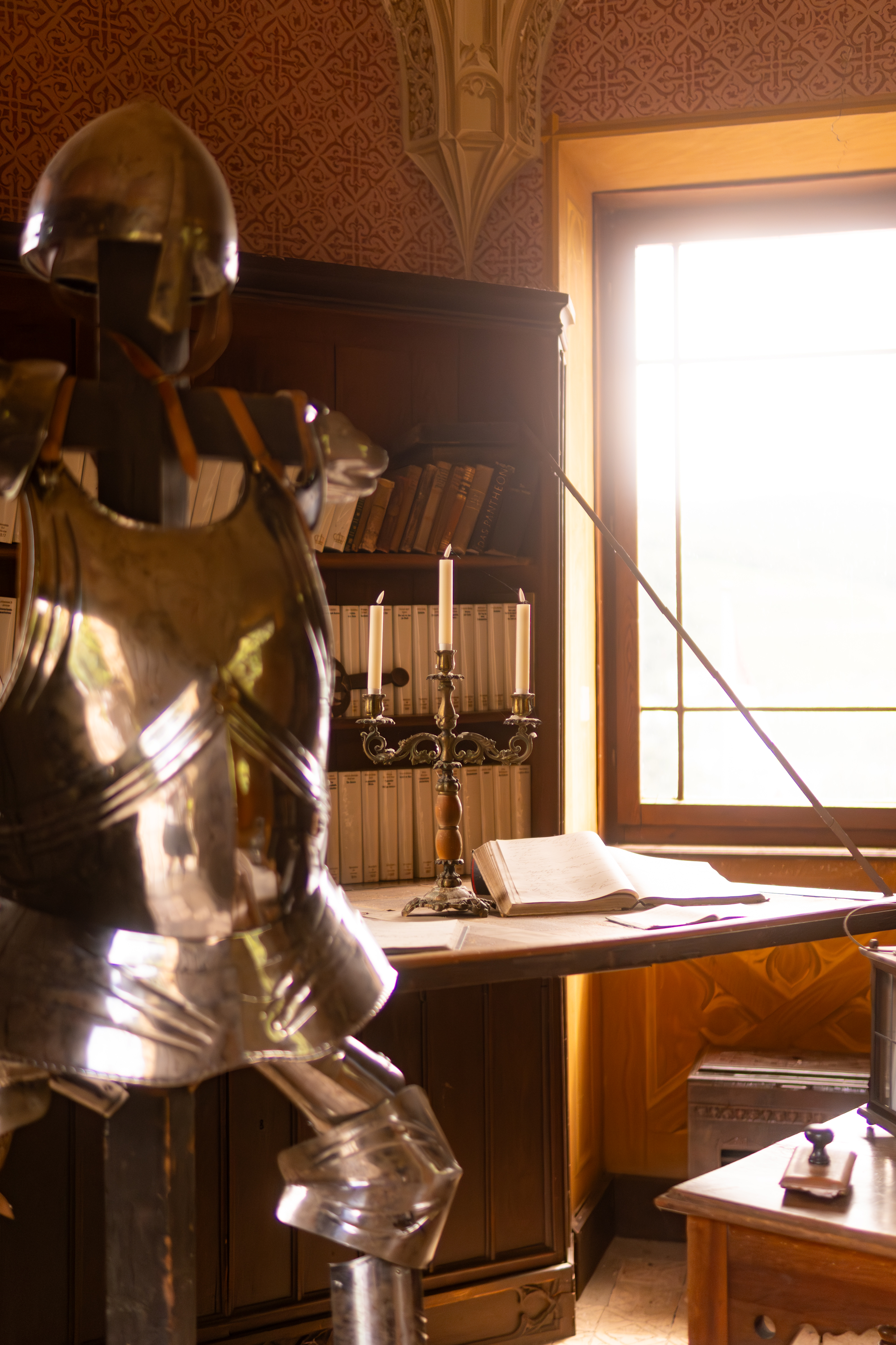 Ritterrüstung, dreiflammiger Kerzenständer, aufgeschlagenes Buch und Bücherregal