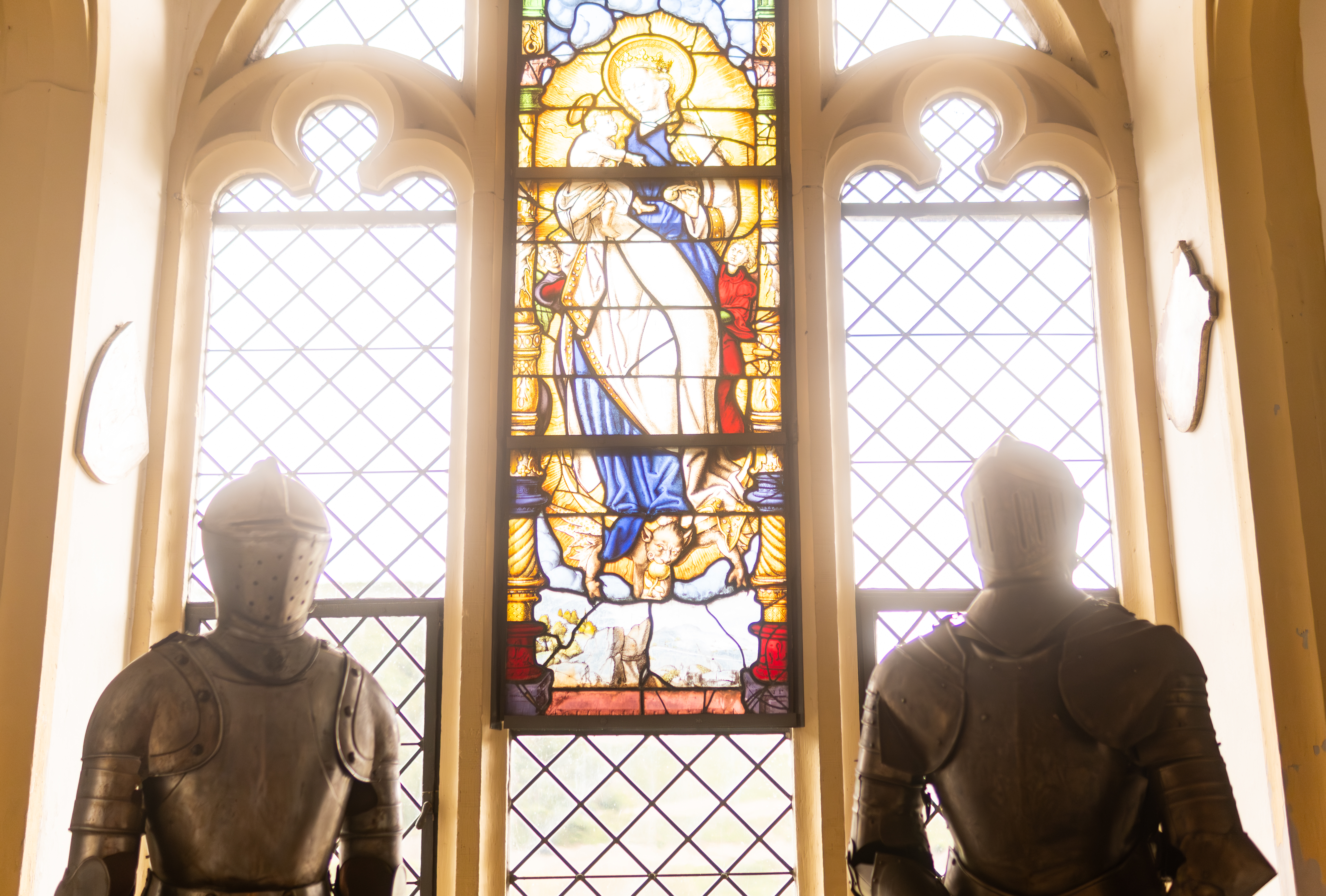 Zwei Ritterrüstungen vor farbigem Kirchenfenster, gleißendes Licht